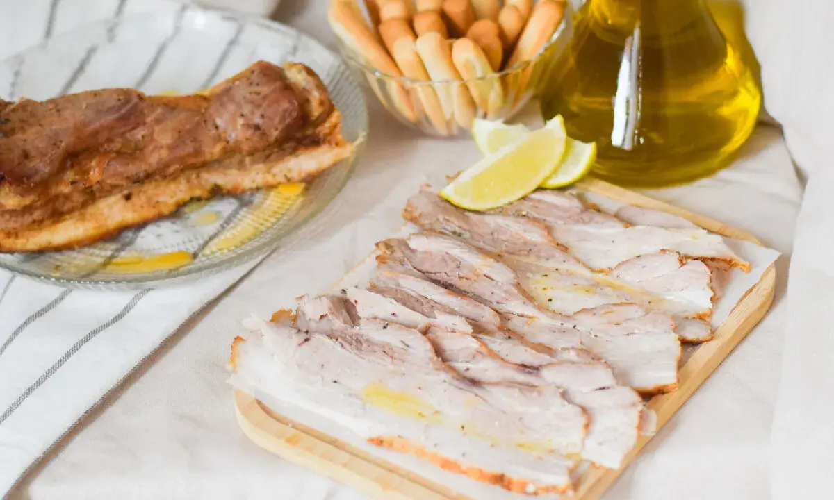 Chicharrón de Cádiz, lonchas de panceta crujiente, limones y palitos de pan, listos para disfrutar.