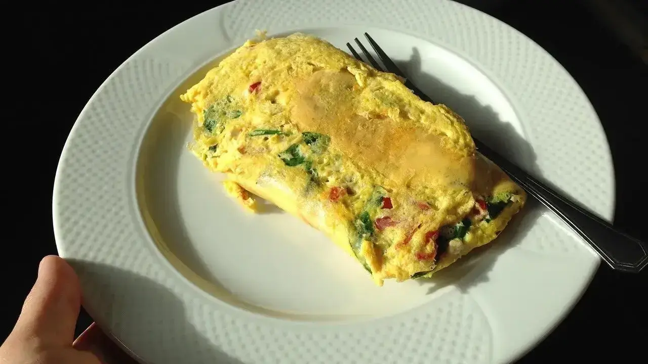 Pyszne śniadanie na redukcji: omlet z warzywami na białym talerzu, gotowy do zjedzenia.