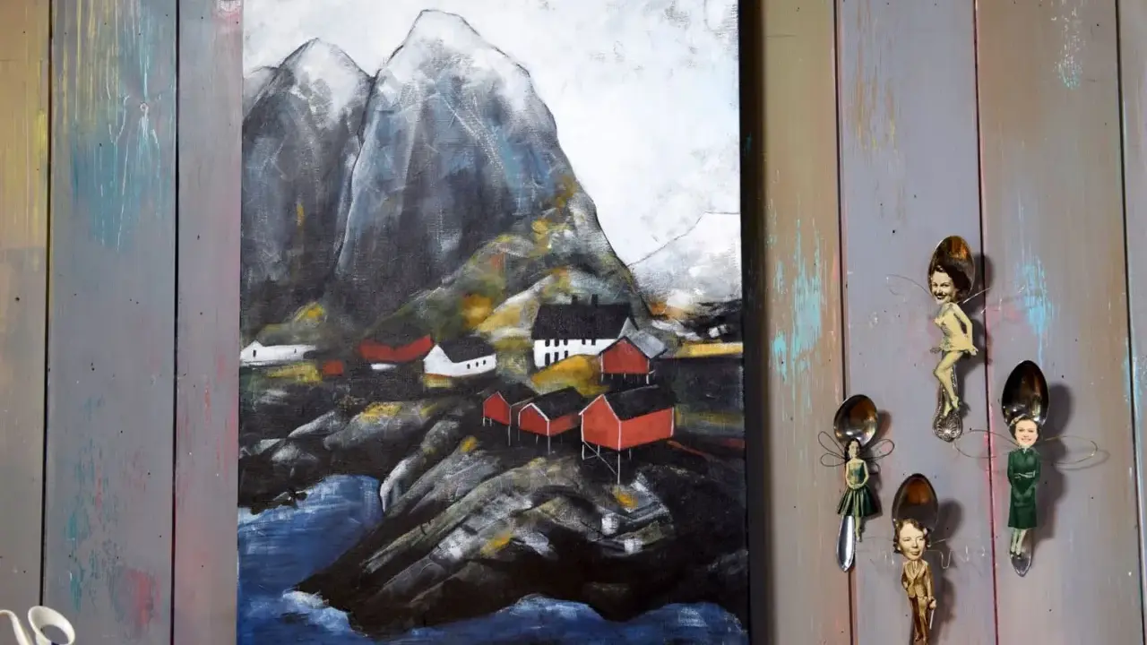 Målade landskap med röda hus vid en bergig kust. Konstverket hänger på en vägg av slitna träplankor.