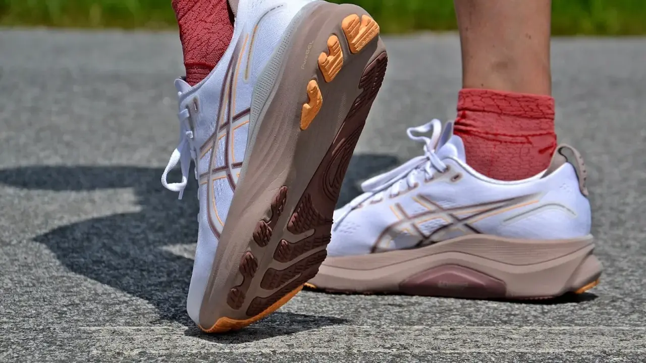 Białe buty do biegania z pomarańczowymi akcentami i charakterystycznym logo. To właśnie asics co to za firma, znana z innowacyjnych rozwiązań dla sportowców.