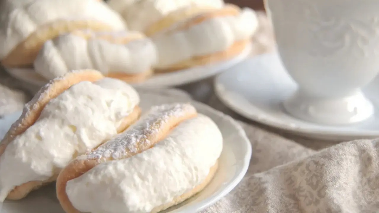 Puszyste ciasteczka przełożone obfitą porcją bitej śmietany, niczym delikatny omlet z bitą śmietaną, kuszą na talerzyku.