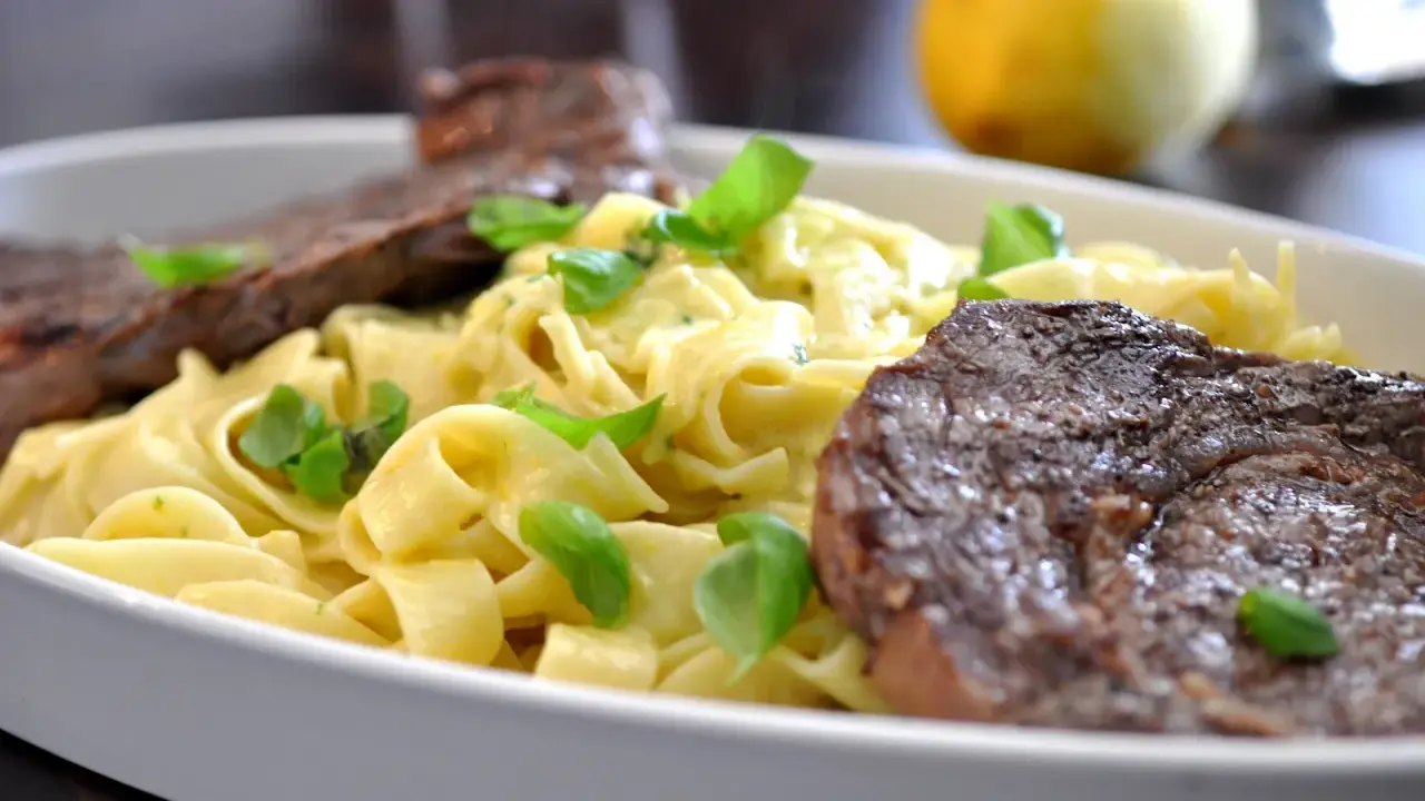 En krämig pastarätt med tagliatelle, garnerad med färsk basilika och serverad med saftig entrecote.