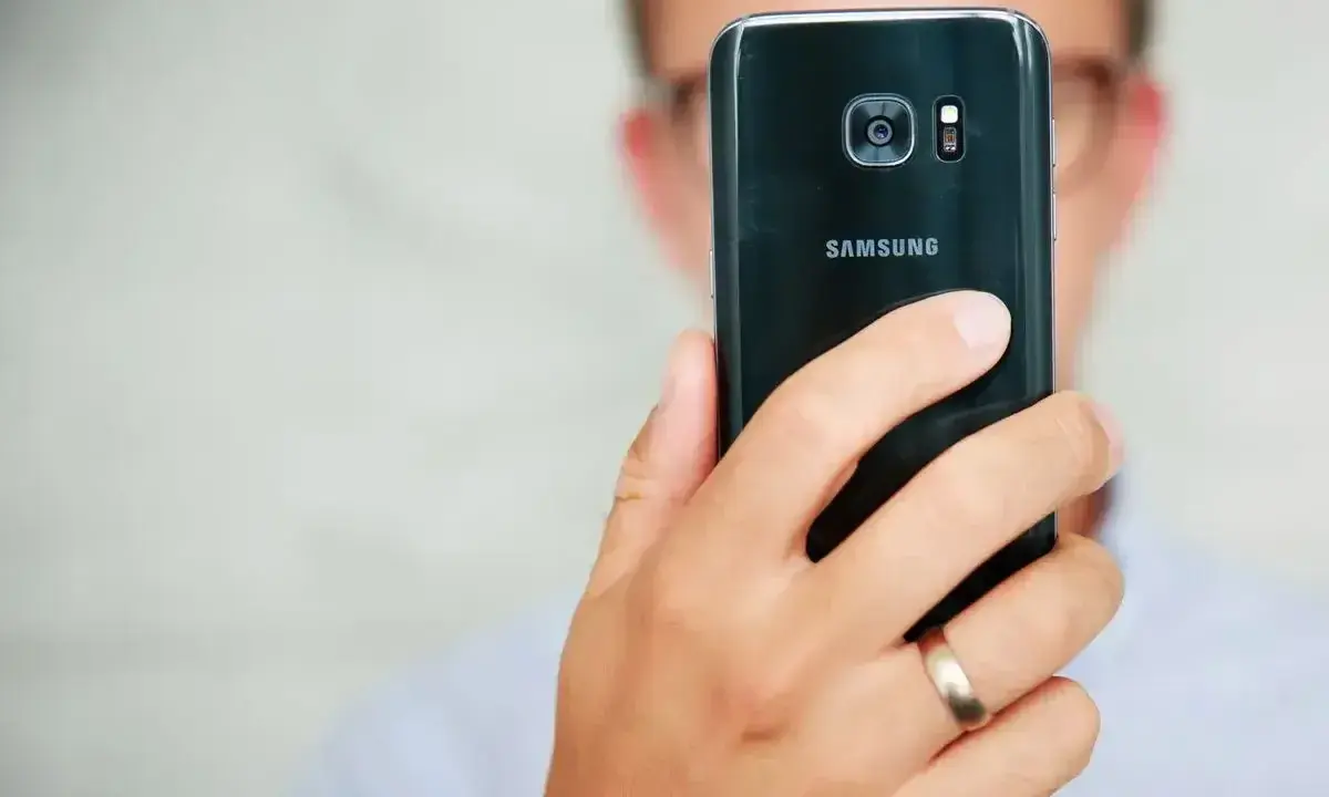Osoba trzyma czarny telefon Samsung, pokazując tył z aparatem. Dowiedz się, jak poprawić jakość aparatu w telefonie Samsung, aby robić lepsze zdjęcia.
