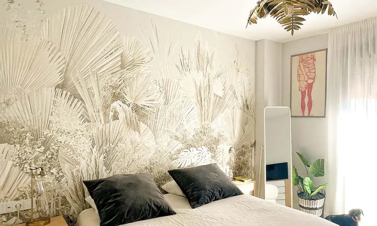 Dormitorio con papel pintado de palmeras, ideal para aprender como poner papel pintado. Cama con cojines oscuros, espejo y planta.