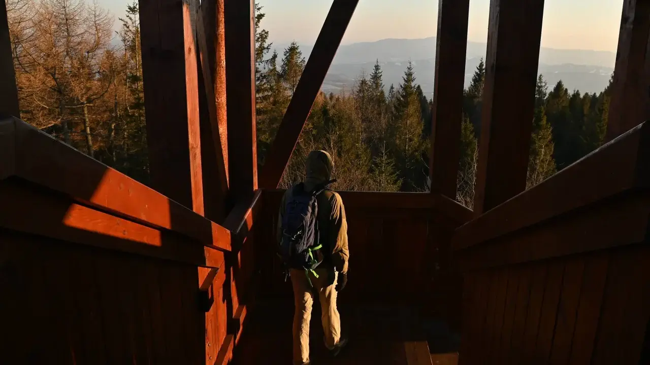 Turysta wchodzi po drewnianych schodach na wieżę widokową, podziwiając panoramę gór.
