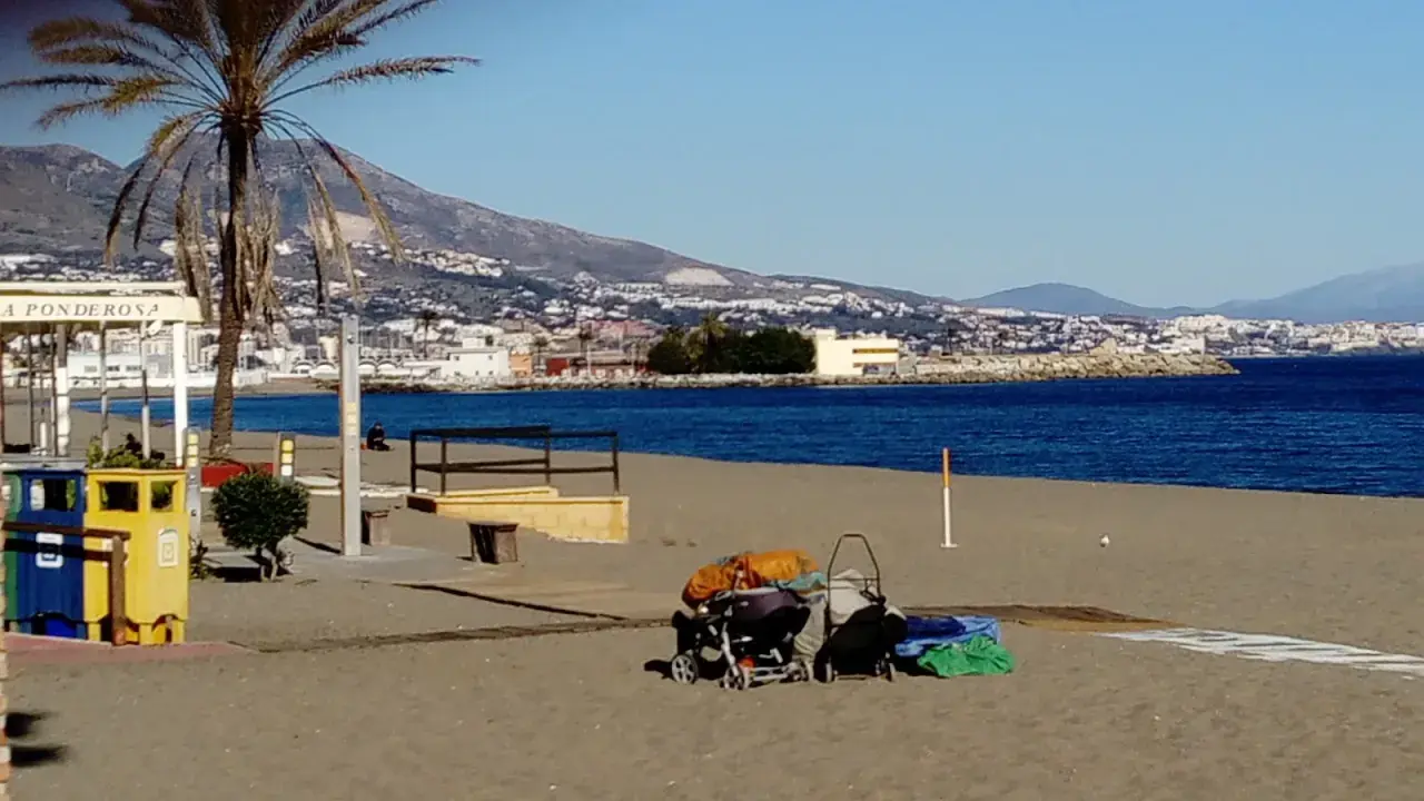 Sonniger fuengirola strand mit Palmen, Bergen und dem Meer im Hintergrund. Kinderwagen und Gepäck liegen am Sand.