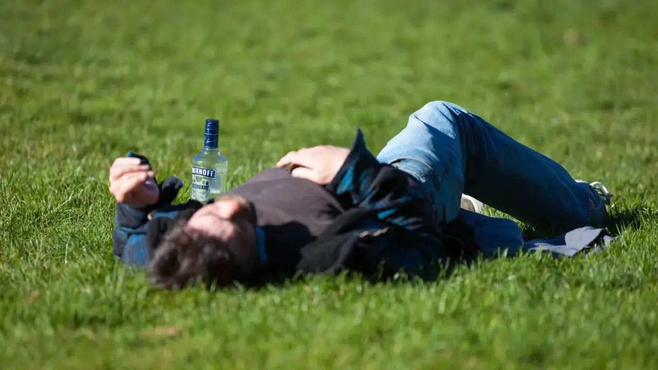 Mężczyzna leży na trawie obok butelki wódki. Czy padaczka alkoholowa jest śmiertelna? To pytanie budzi niepokój.
