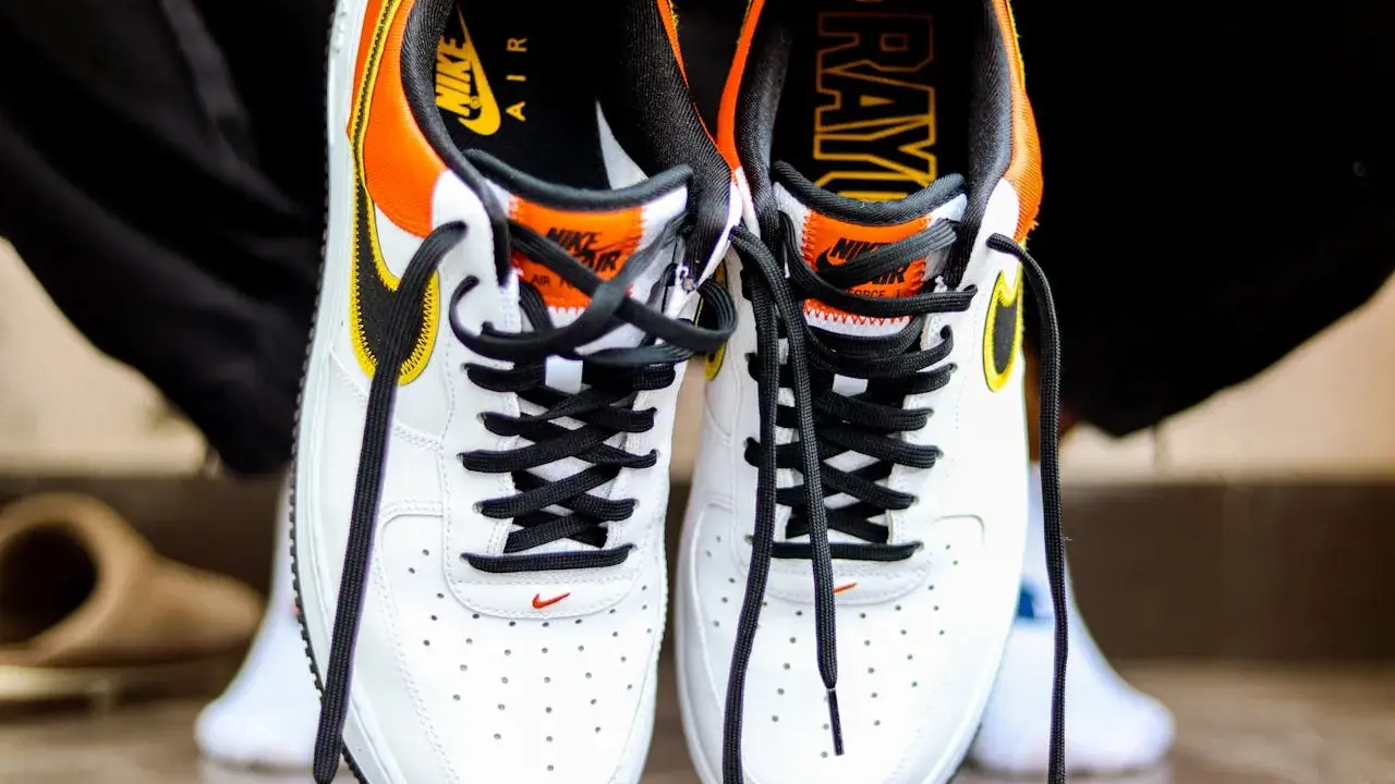 Białe buty Nike Air Force 1 z pomarańczowo-żółtymi akcentami. Sprawdź metkę i logo, by dowiedzieć się, jak sprawdzić czy buty są oryginalne.