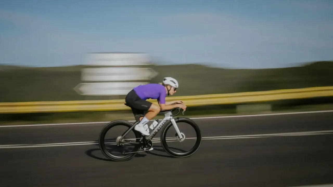 Kolarz w fioletowej koszulce pędzi na rowerze, osiągając prędkość 50 km/h.