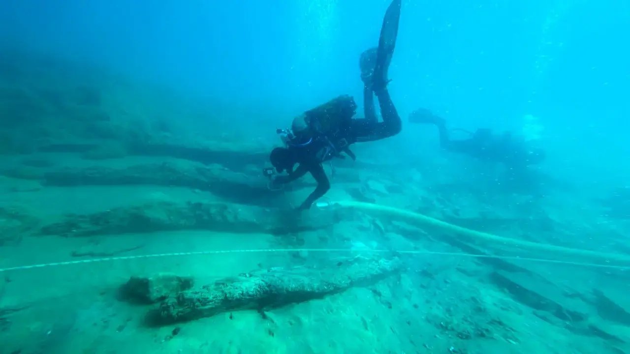 Subacquei esplorano un sito archeologico subacqueo, tra antichi resti di legno. Un'immersione per scoprire cosa vedere.