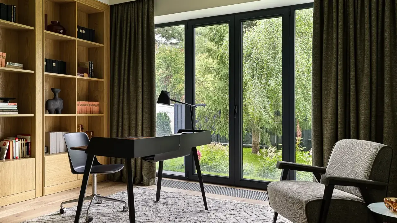 Acogedora habitacion despacho en casa con estanterías de madera, escritorio negro y sillón estampado. Ventanal con vistas al jardín.