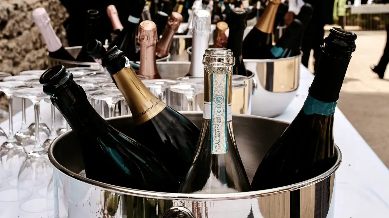 Mehrere Flaschen Sekt in einem silbernen Eiskübel, bereit für die Feier. Gläser stehen daneben.