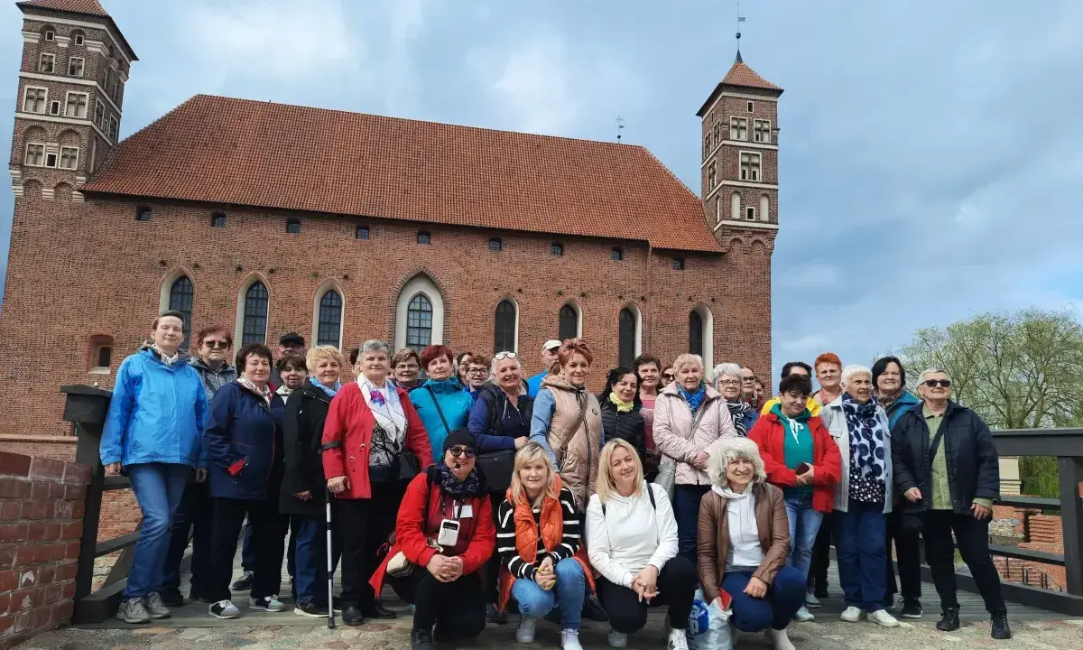 Grupa turystek pozuje na tle imponującego zamku biskupów warmińskich w Lidzbarku Warmińskim.