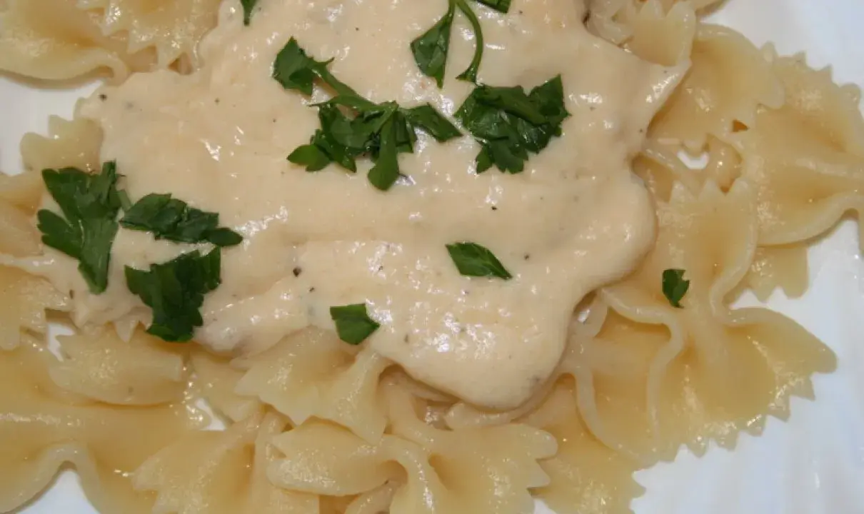 Makaron farfalle polany kremowym sosem serowym i posypany natką pietruszki.