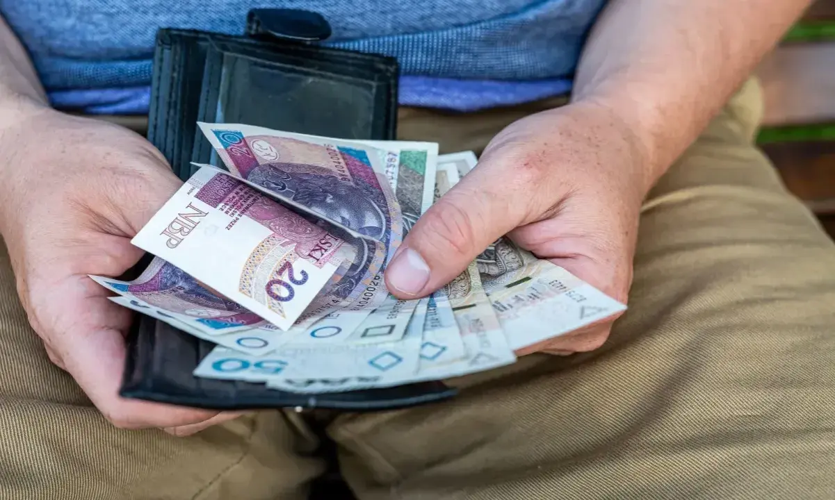 Ręce trzymają portfel z polskimi banknotami. Czy dodatek pielęgnacyjny jest opodatkowany? Pieniądze w portfelu mogą pomóc w odpowiedzi.