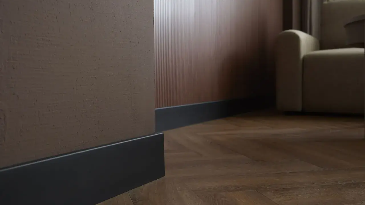 Ciemne listwy przypodłogowe przy brązowej i drewnianej ścianie, na tle parkietu i kanapy.