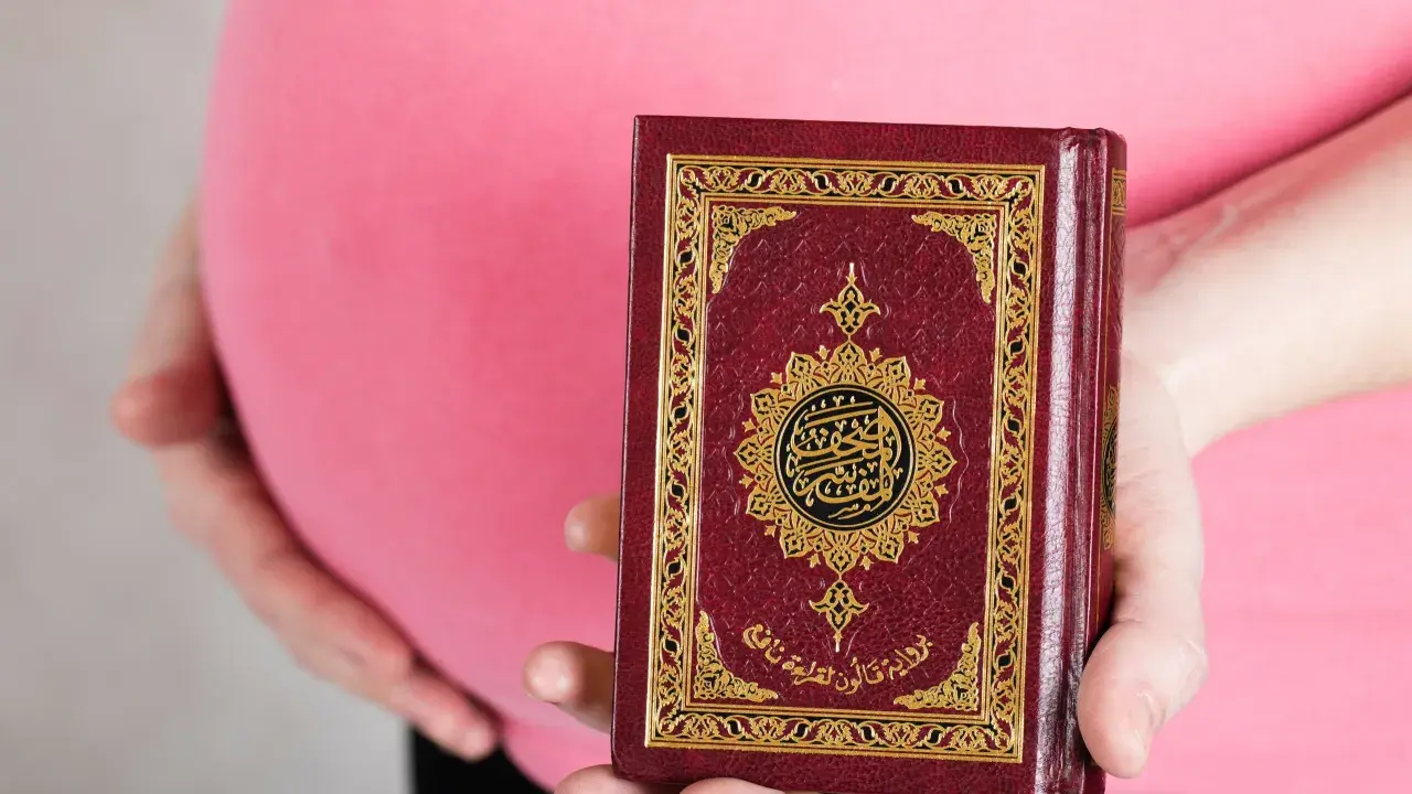 Schwanger, hält eine Frau den Koran. Im Islam gibt es Erleichterungen beim Fasten während der Schwangerschaft.