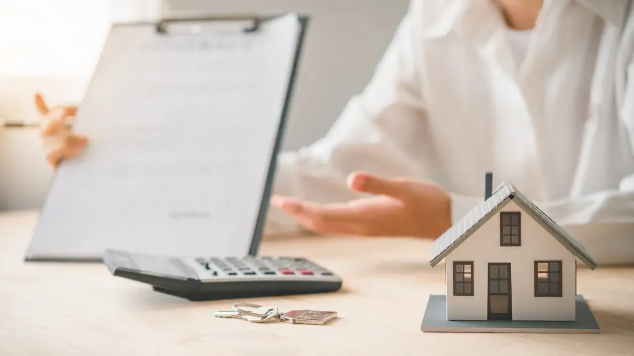 Une personne présente un contrat, une calculatrice, des clés et une maquette de maison. L'ambiance est un peu sinistre, comme si un problème était sur le point d'être révélé.