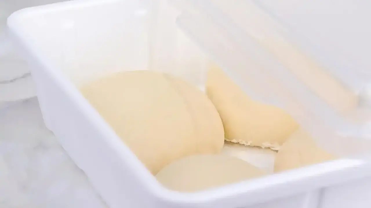 Pâte à pain trop fermenté dans une boîte blanche, prête pour la cuisson.