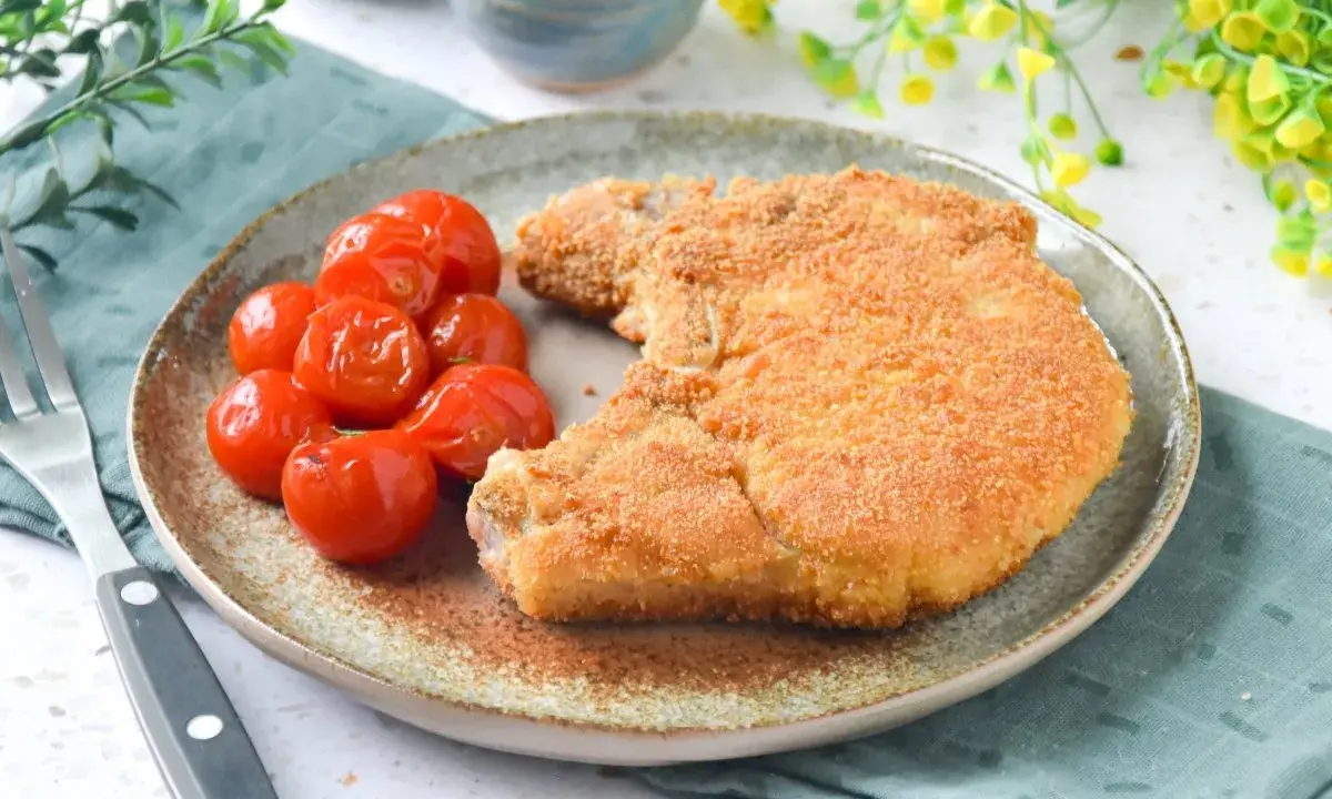 Cotoletta alla milanese dorada y crujiente, acompañada de tomates cherry asados. Un plato clásico y delicioso.