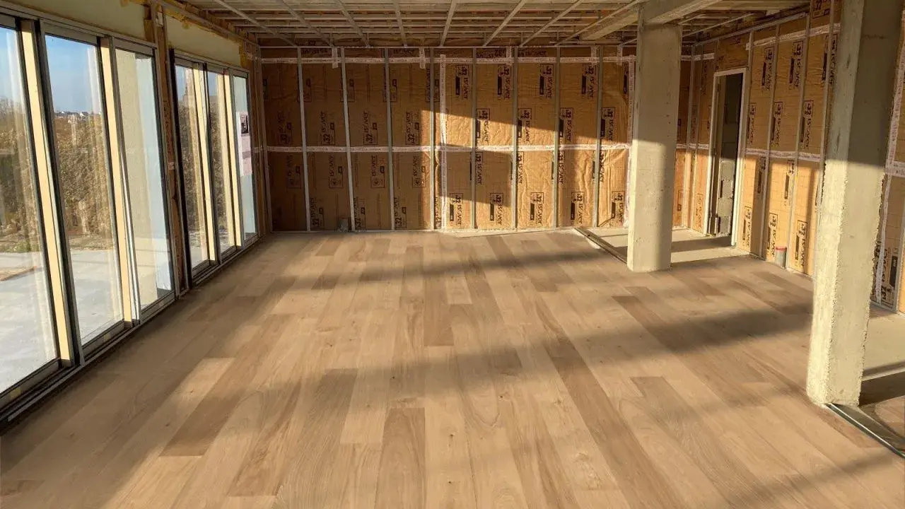 Pose de parquet clair dans une pièce en construction, le sens des lames semble agrandir l'espace.