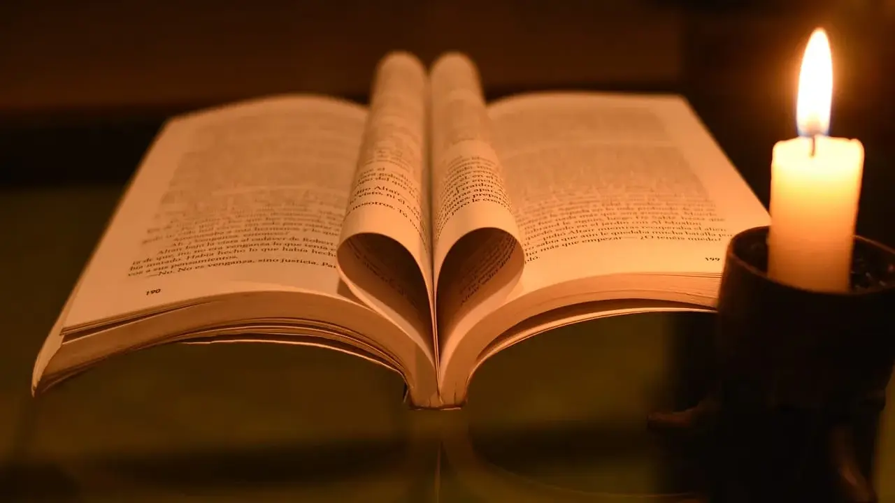 Otwarta księga z kartkami uformowanymi w serce, obok płonąca świeca. W świetle świecy czytam psalm 37 1-4.