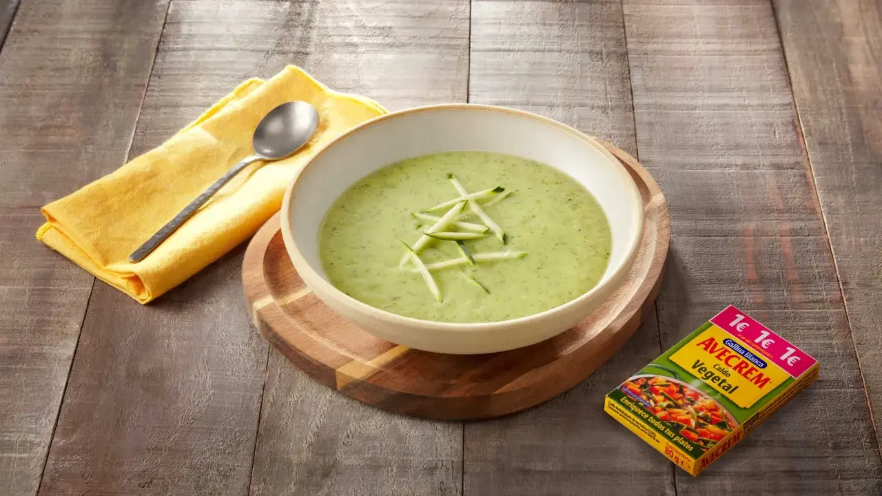 Crema de calabacín para niños, servida en un cuenco blanco sobre tabla de madera. Al lado, un paquete de caldo vegetal Avecrem.