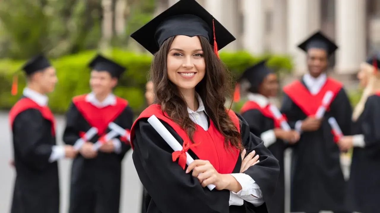 Uśmiechnięta absolwentka z dyplomem w ręku, w tle inni studenci po ang.