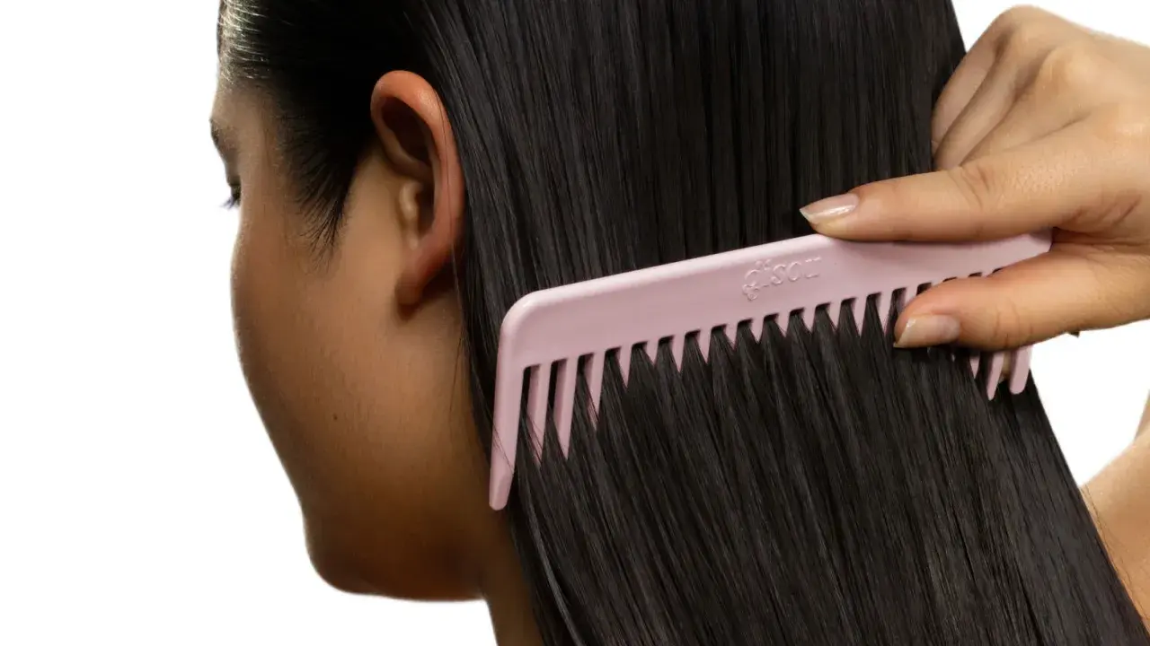 Une main peigne des cheveux noirs et brillants avec un peigne rose. Le peigne est large et espacé, idéal pour démêler les cheveux sans les casser, évitant ainsi les cheveux emmêlés cause.