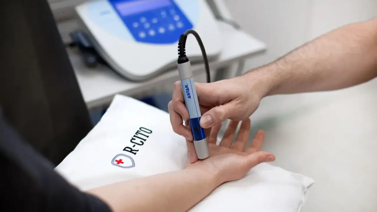 Fizjoterapeuta wykonuje zabieg laserem na dłoni pacjenta.