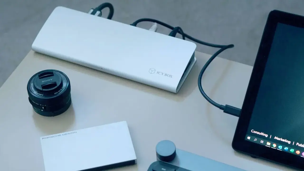 Stacja dokująca ICY BOX podłączona do laptopa, obok obiektyw Sony i dysk Porsche Design.