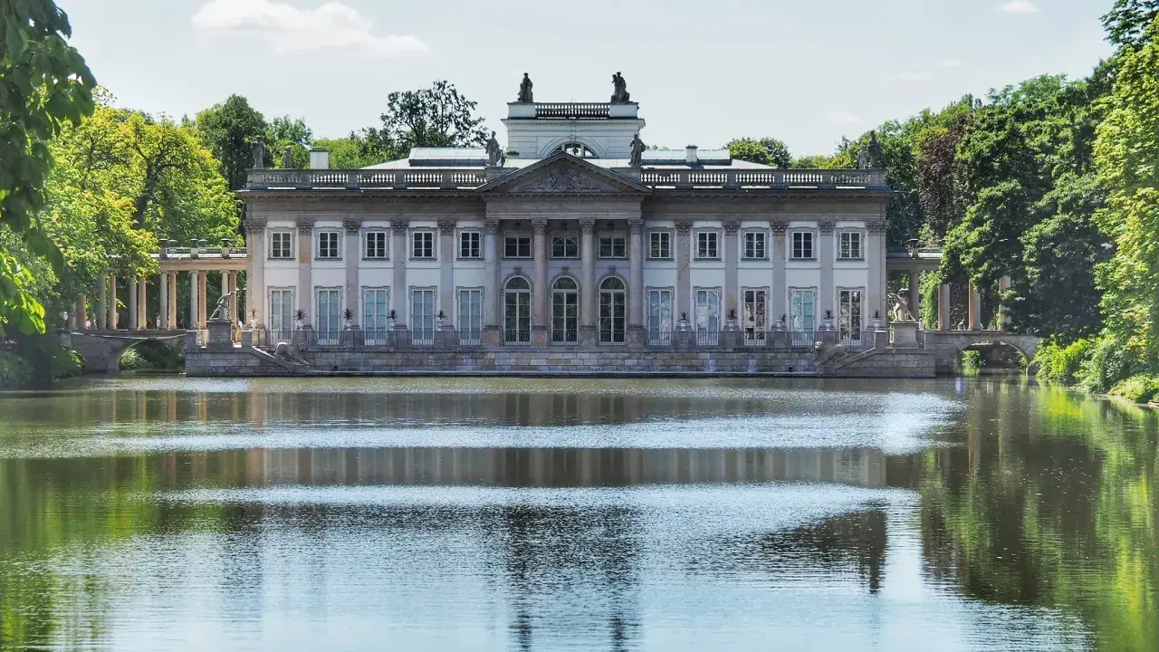 Pałac na Wodzie w Łazienkach Królewskich odbija się w spokojnej tafli jeziora, otoczony zielenią drzew.