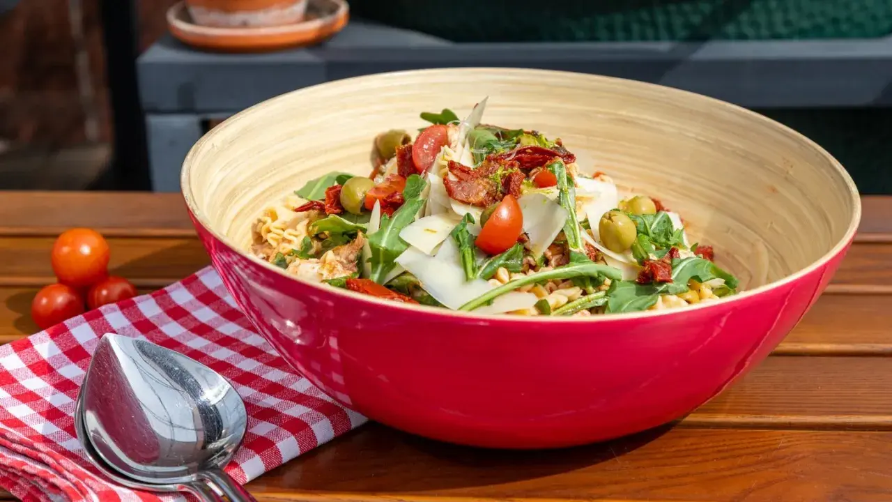 Leckere nudelsalat ideen: Pasta mit Rucola, Tomaten, Oliven und Parmesan in einer roten Schüssel.