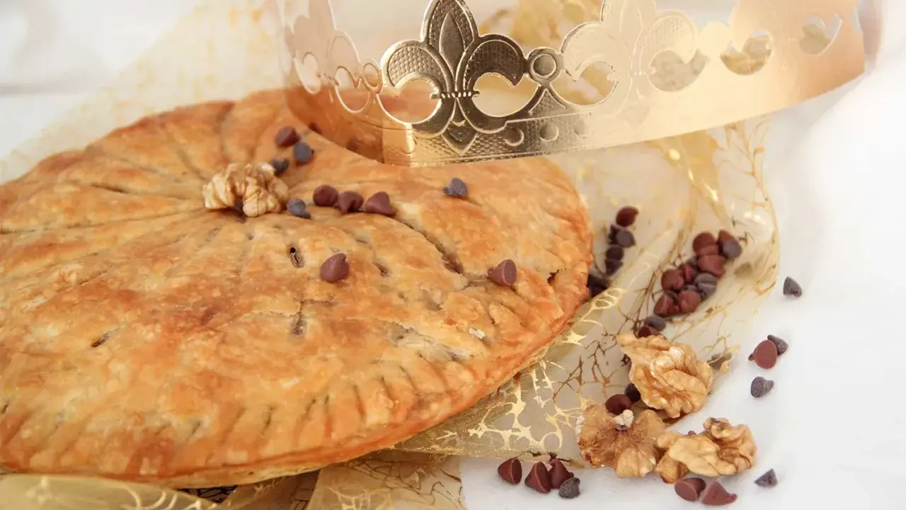 Une galette des rois pépite de chocolat dorée, parsemée de pépites de chocolat et de noix, sous une couronne royale.