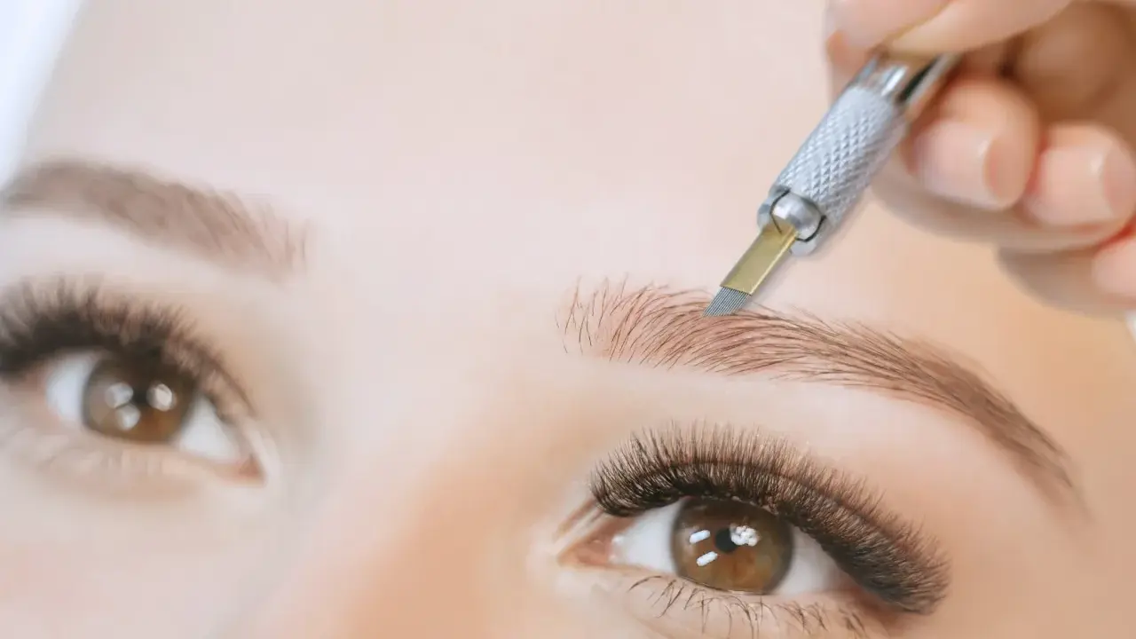 Main d'une esthéticienne réalisant un microblading poil à poil sur un sourcil.