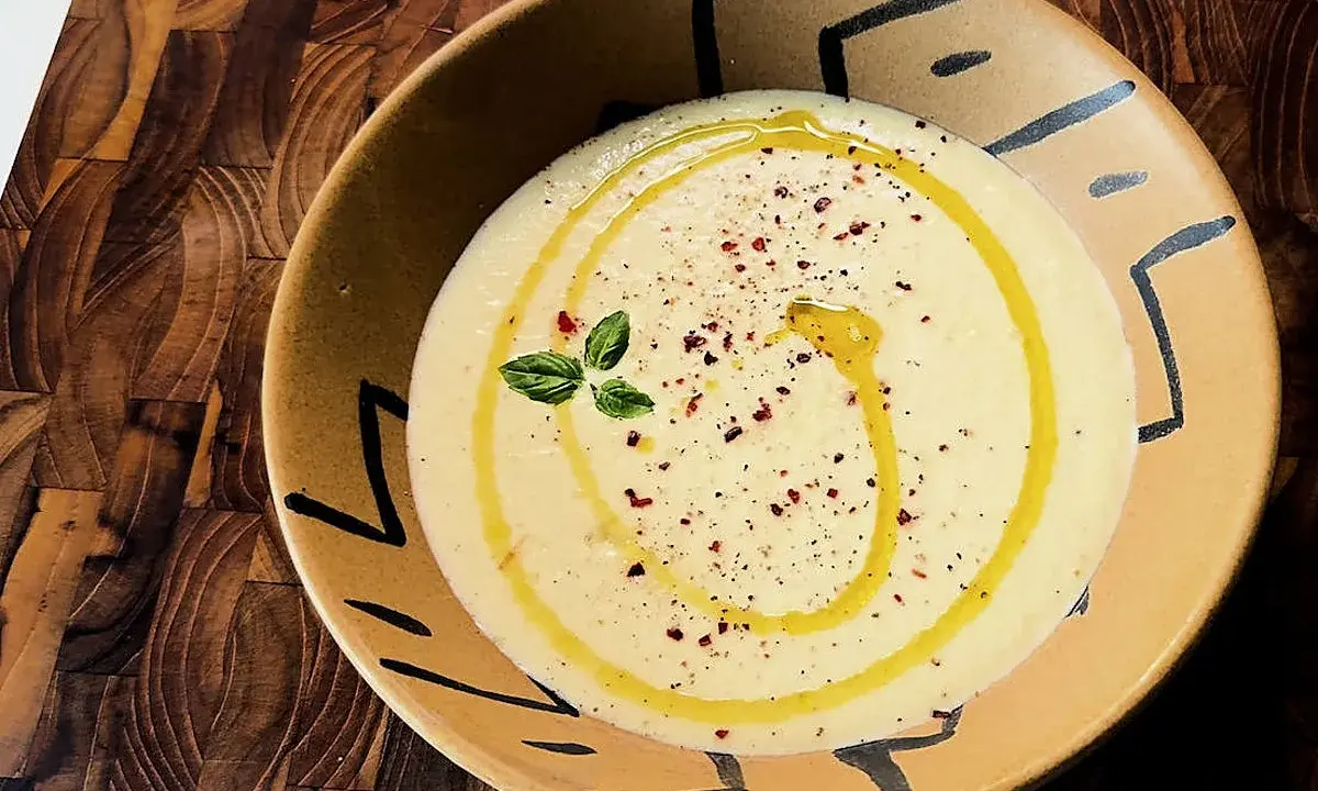Gazpacho de calabacín cremoso, con un hilo de aceite de oliva, pimentón y una ramita de albahaca, servido en un cuenco artesanal.