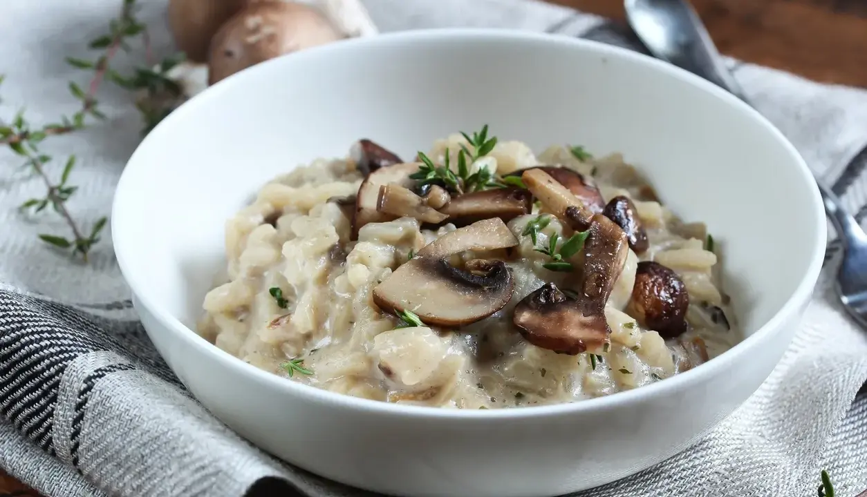 Aksamitne risotto z pieczarkami, udekorowane świeżym tymiankiem, w białej misce na lnianej serwetce.