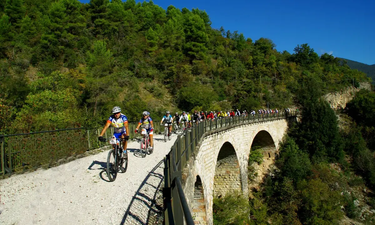 Ciclisti in gruppo percorrono la ciclabile Spoleto Norcia su un viadotto panoramico, immersi nel verde.