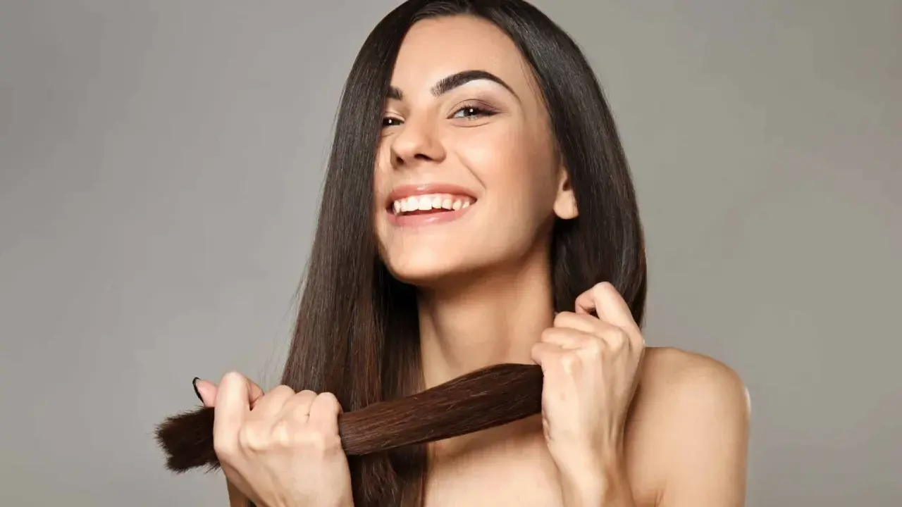 Mujer sonriente muestra su cabello largo y sedoso, un ejemplo de cómo cuidar el pelo para que luzca saludable y brillante.