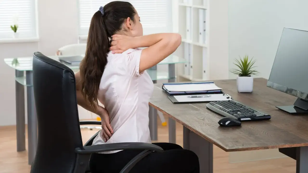 Femme souffrant de douleurs au cou et au dos à son poste de travail. Le travail sédentaire peut causer des problèmes de santé.