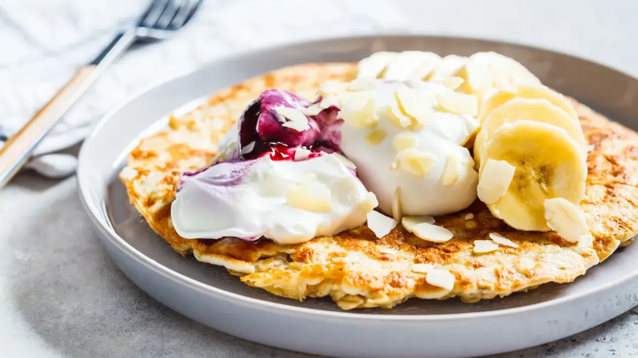 Puszysty omlet z jogurtem, jagodami, bananem i płatkami migdałów. Idealny przepis na zdrowy omlet na śniadanie.