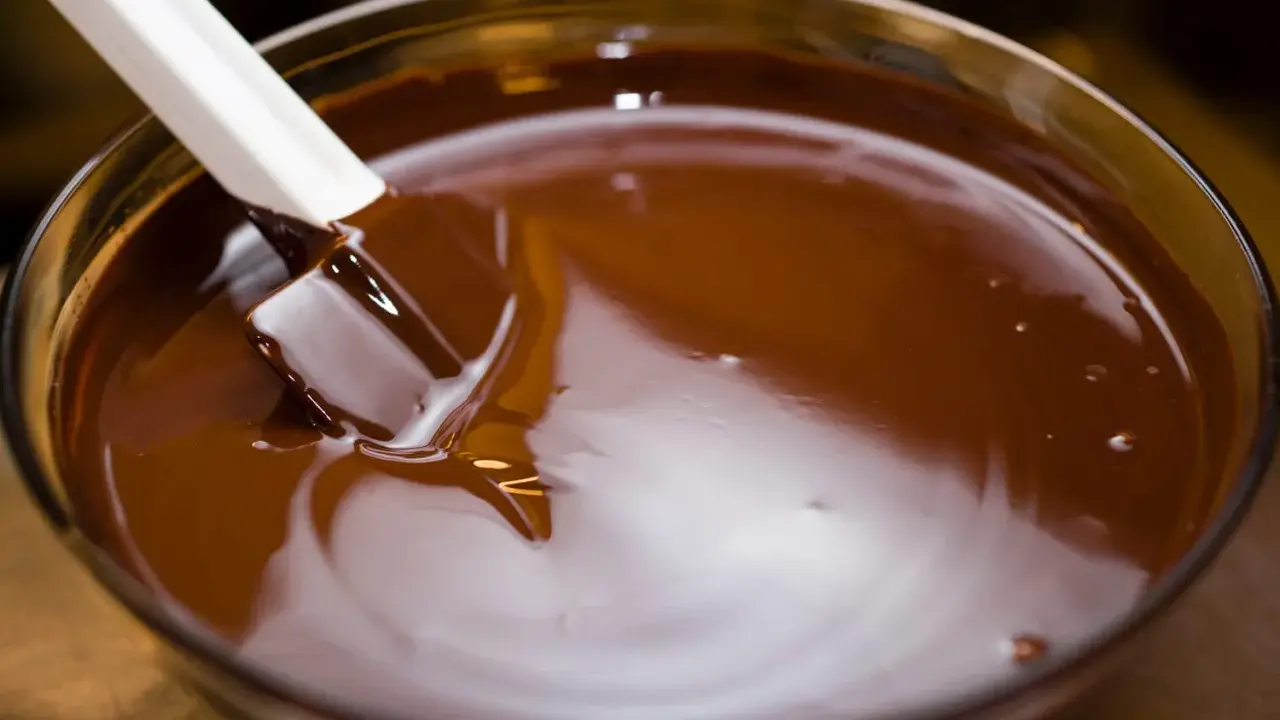 Spatule blanche remuant du chocolat fondu dans un bol en verre. Le chocolat est lisse et brillant, prêt à être utilisé pour une recette.