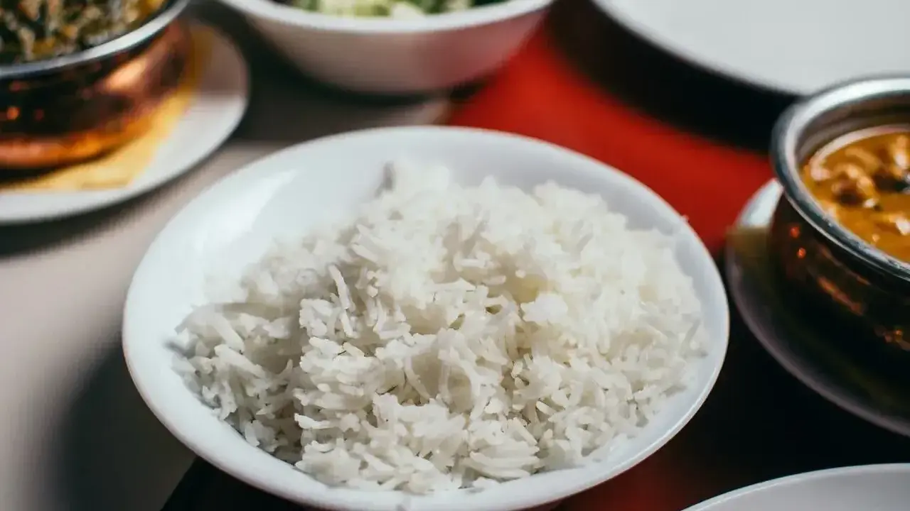 Biały ryż, źródło węglowodanów, w misce obok indyjskiego curry i sałatki.