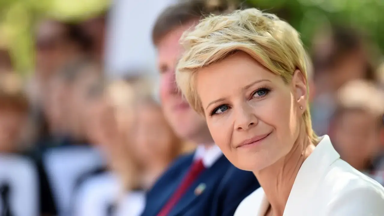 Kobieta z blond włosami w super krótkiej fryzurze damskiej, w białej marynarce, uśmiecha się.