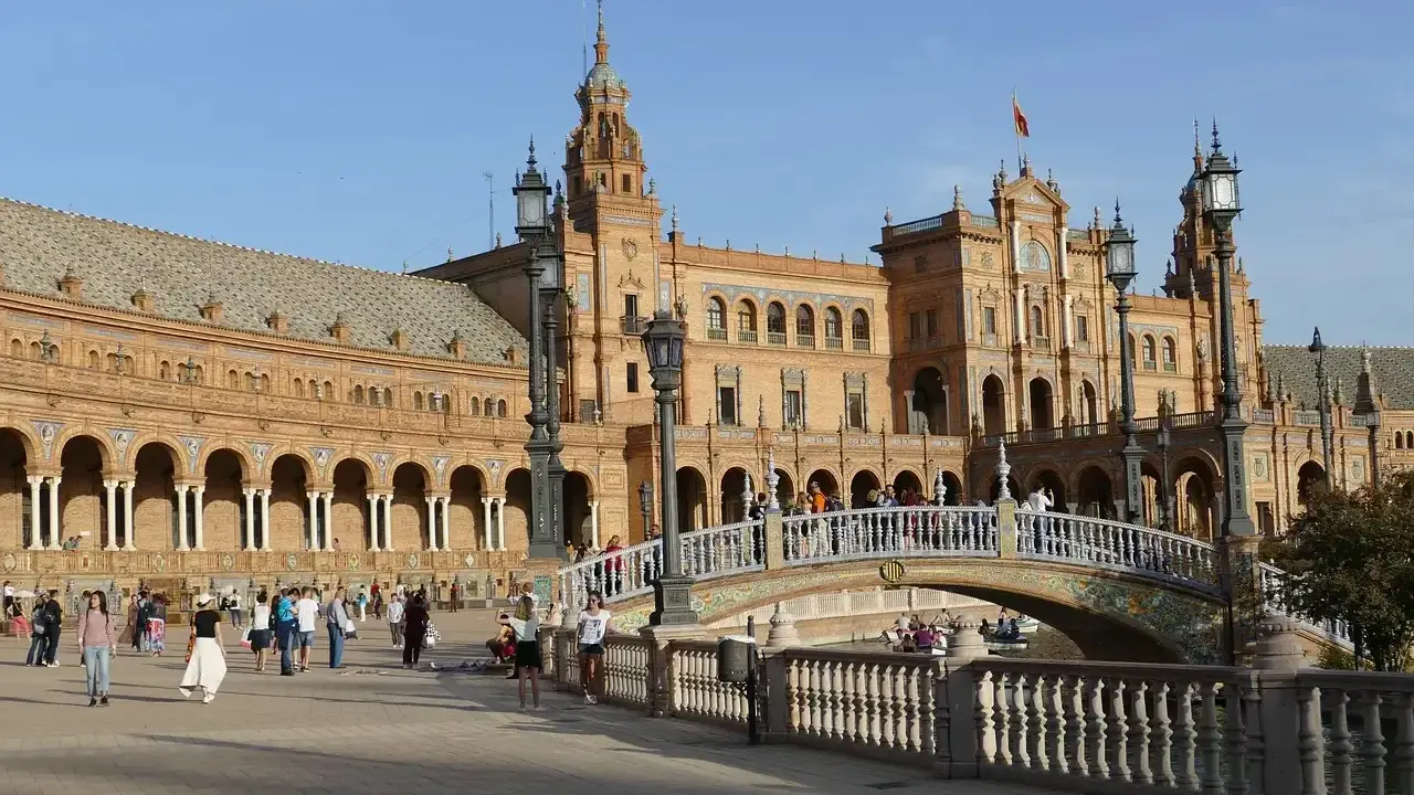 Familien genießen einen sonnigen Tag auf der Plaza de España in Sevilla. Kinder lachen, während sie über die Brücke spazieren, die über einen Kanal führt.