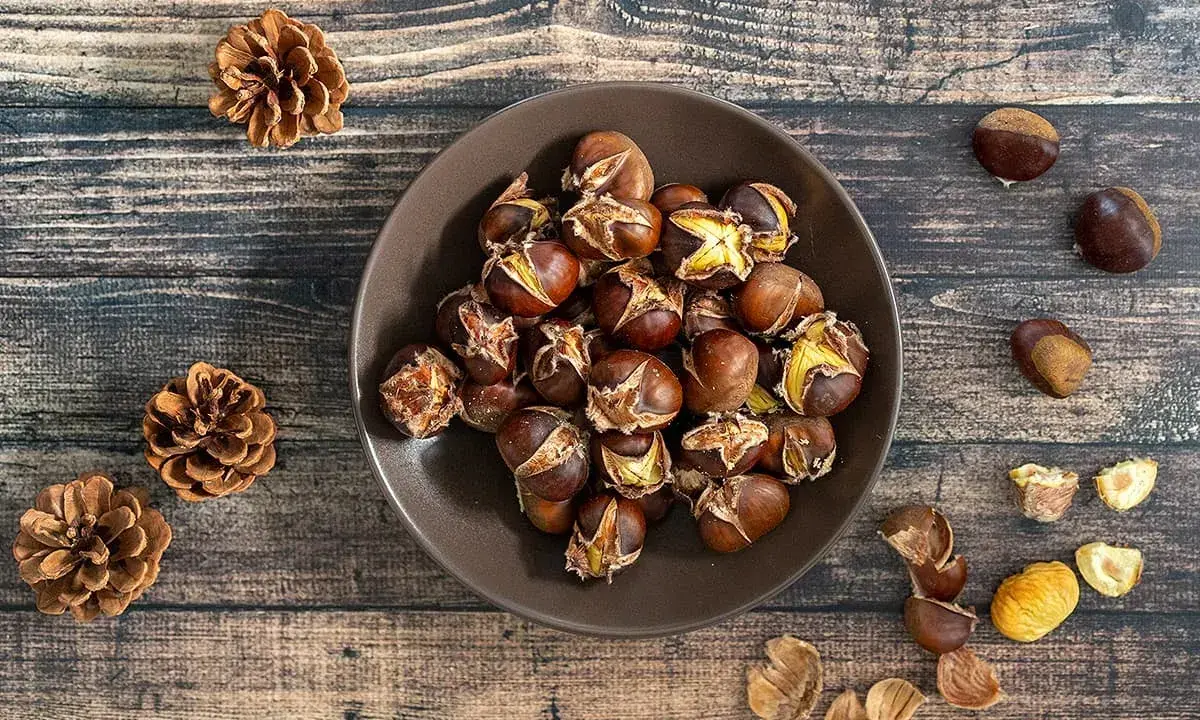 Châtaignes grillées dans un bol, sur fond de bois, avec des pommes de pin.