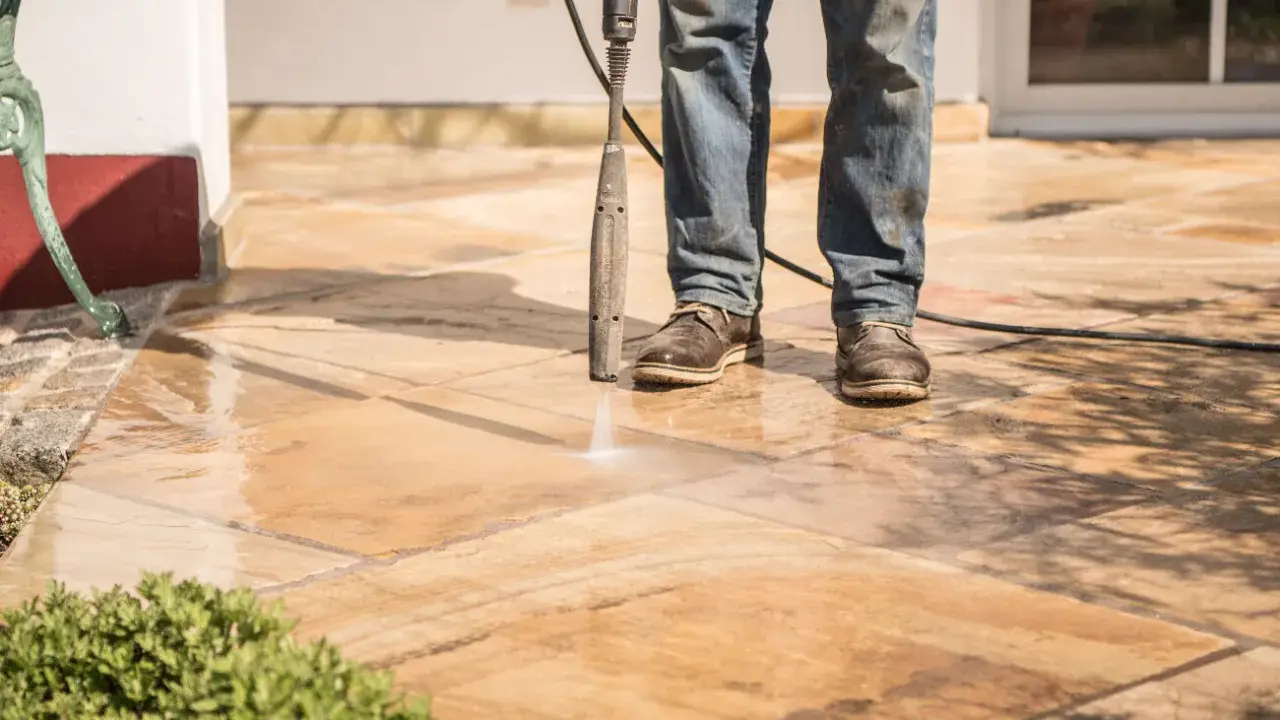 Nettoyer carrelage extérieur noirci avec un nettoyeur haute pression. L'eau projetée révèle la beauté naturelle des dalles.