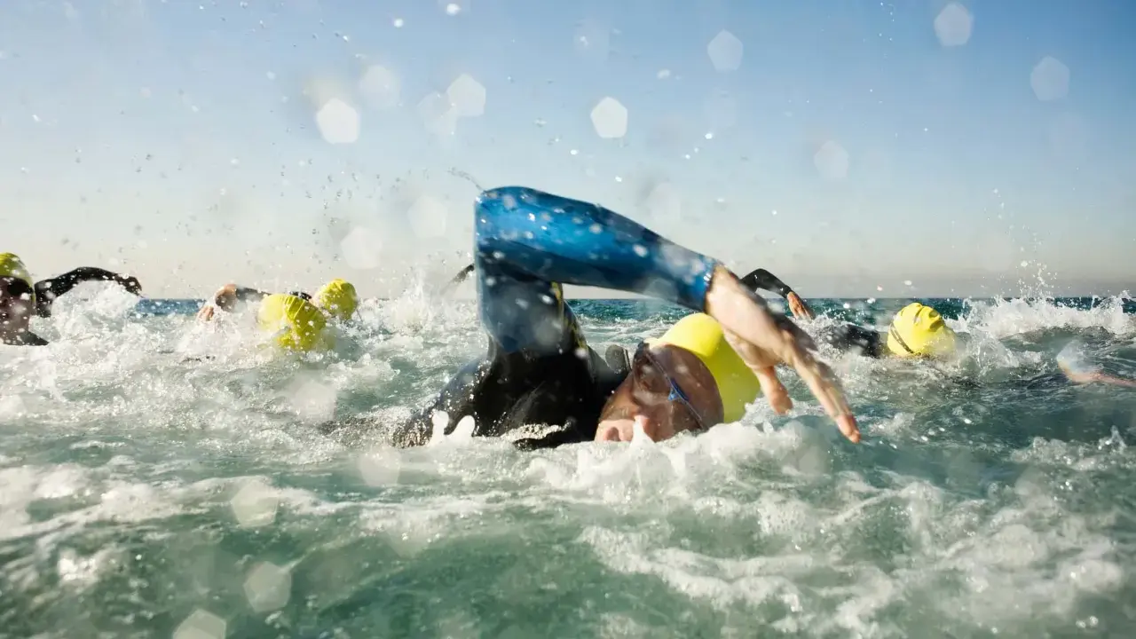 Schwimmer mit gelben Kappen kämpfen sich durch die Wellen. Die triathlon strecken sind anspruchsvoll.