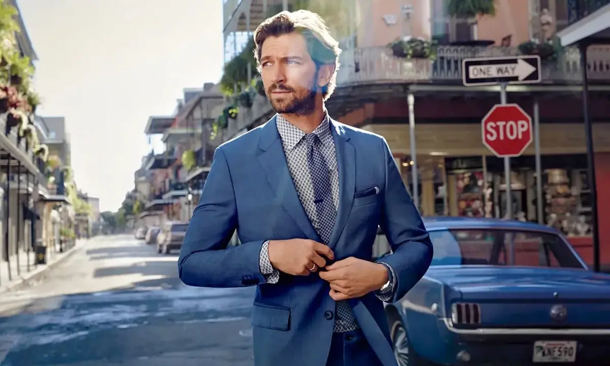 Man in a sharp blue suit, ready for a business cocktail, stands on a street with a vintage car and classic architecture.