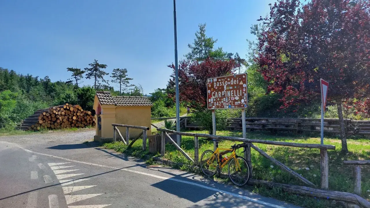 Bicicletta gialla appoggiata alla staccionata al Passo dei Carpinelli, con un cartello che indica l'altitudine e un piccolo edificio.